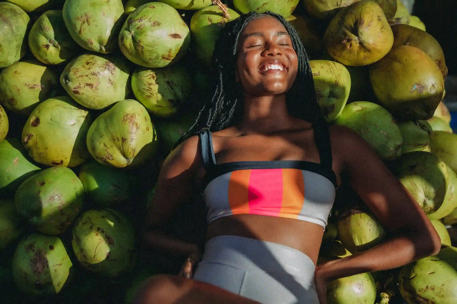Mulher sorrindo em frente a cocos com top colorido